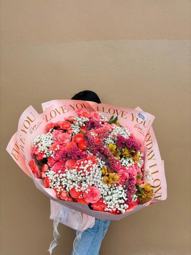 A vibrant bouquet with coral-pink roses, yellow alstroemerias, white baby’s breath, and purple celosia.