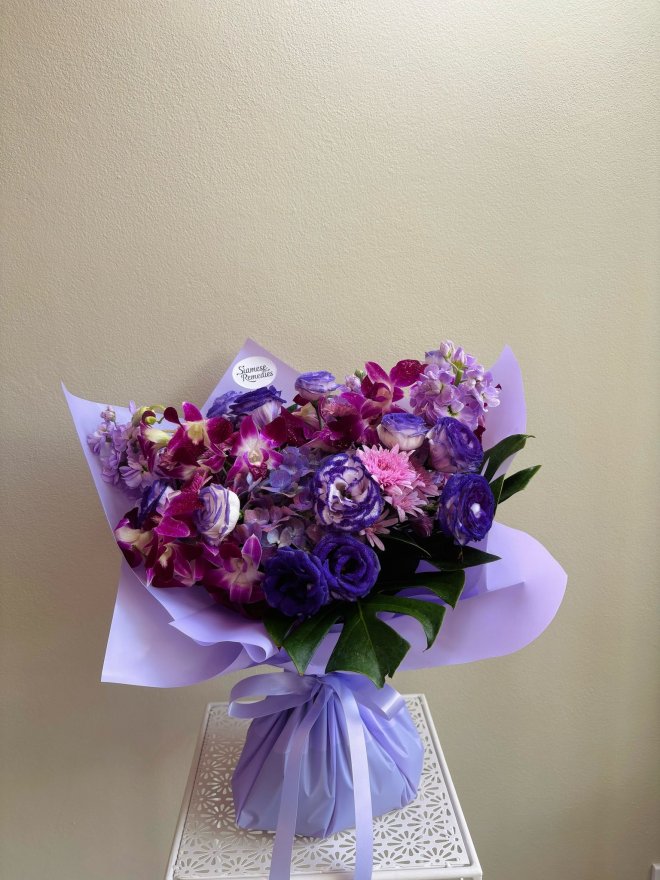 Purple-themed bouquet with dendrobium orchids, carnations, lisianthus, and lavender wrapping paper.