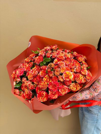 A large bouquet of red and yellow marbled spray roses wrapped in red-orange paper.