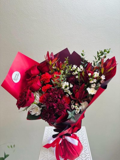 Velvet Flame is a dramatic arrangement of roses, chrysanthemums, and waxflowers in red and burgundy tones.
