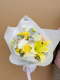 A fresh and cheerful bouquet with yellow lilies and roses, white blooms, and pastel accents, wrapped in soft white paper.