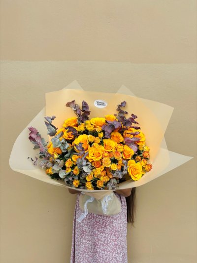 A bouquet of yellow roses with bronze eucalyptus wrapped in soft beige paper.