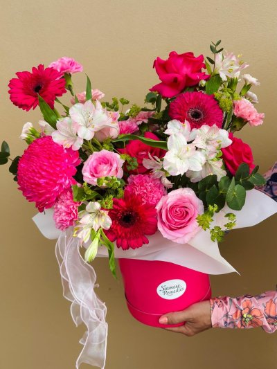 A bright pink bloom box filled with roses, gerberas, carnations, and white lilies.
