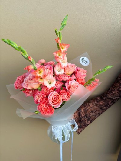 A coral and white bouquet with garden roses, pink roses, white chrysanthemums, and green lisianthus, wrapped in terracotta paper with a gold ribbon.
