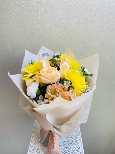 Bouquet of yellow tulips, pale yellow carnations, and pink roses wrapped in green paper with a pink ribbon