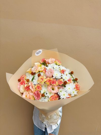 A bouquet of peach lisianthus, coral carnations, and white chrysanthemums wrapped in soft beige paper.