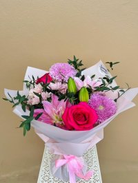 A pink-wrapped bouquet featuring hot pink roses, pink lilies, and purple chrysanthemums.