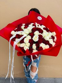 A large bouquet of red and white roses wrapped in red paper, held by someone wearing ripped jeans.