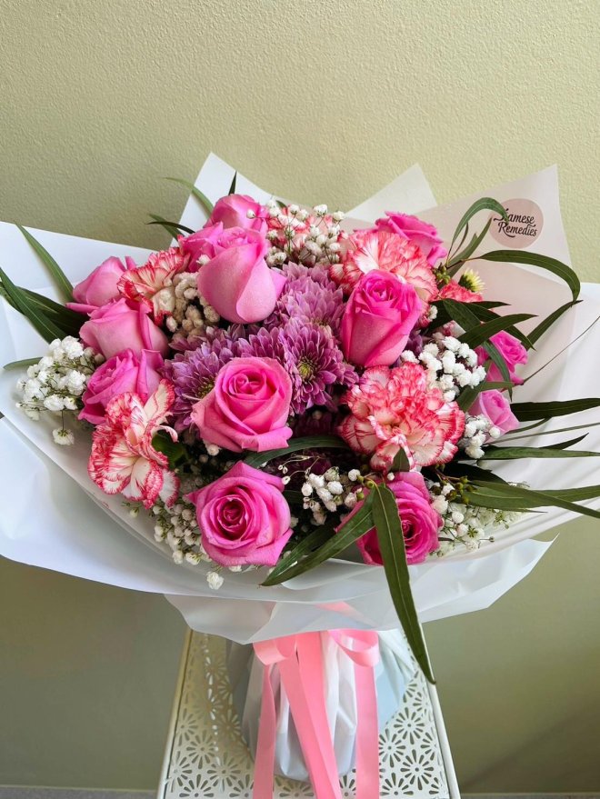 Bouquet of hot pink roses, white and pink carnations, lavender chrysanthemums, and baby’s breath wrapped in white paper with pink satin ribbons