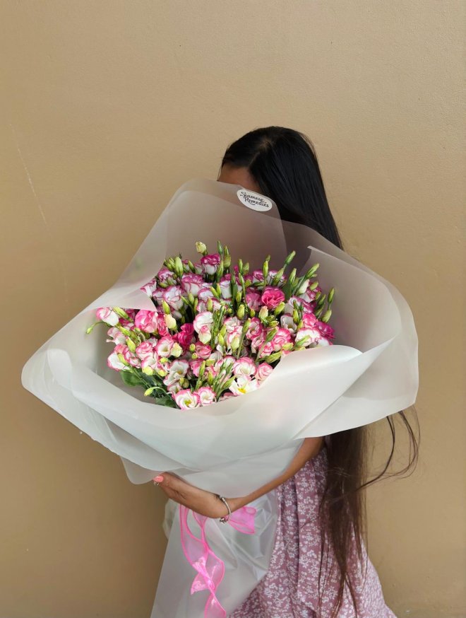 A sheer white-wrapped bouquet of pink and white lisianthus with a flowing pink ribbon.