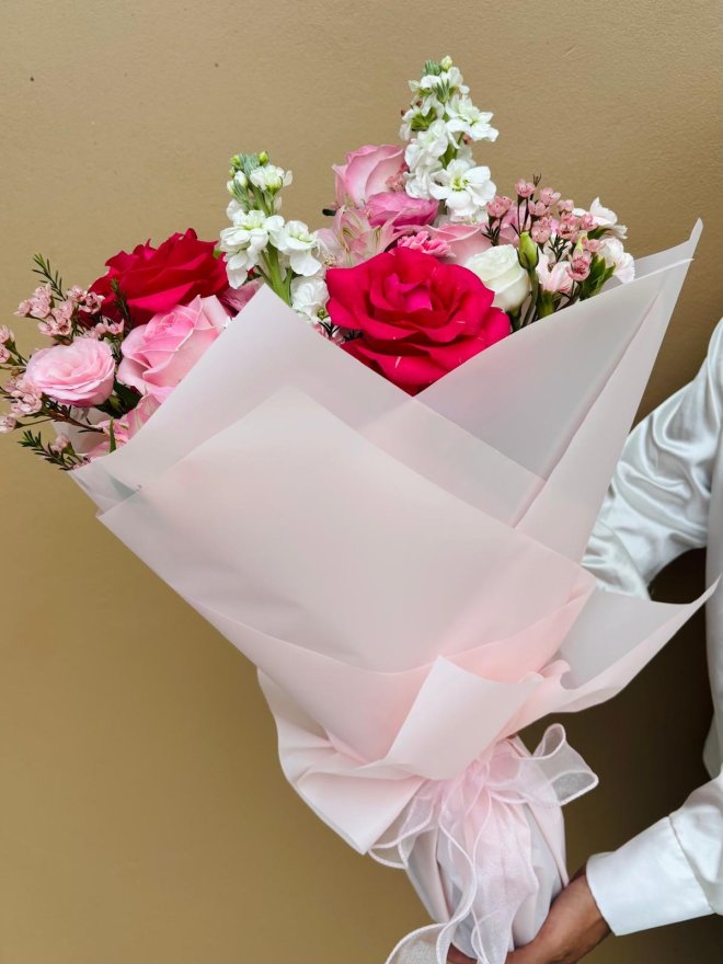 A champagne bottle topped with a floral arrangement of pink roses, lisianthus, and wax flowers.