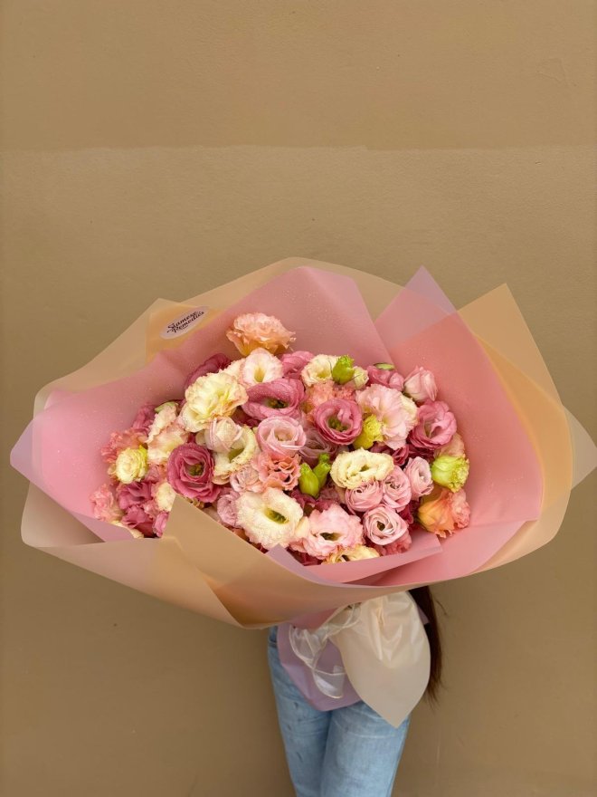 A pastel bouquet of pink, cream, and peach lisianthuses wrapped in blush and champagne paper.
