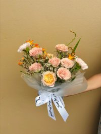 A small bouquet with apricot and peach roses, white wax flowers, orange dry flowers, and light carnations wrapped in frosted white.