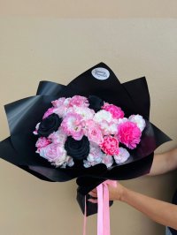 A dramatic bouquet of black, pink, and white roses with carnations and lisianthuses in black wrapping.