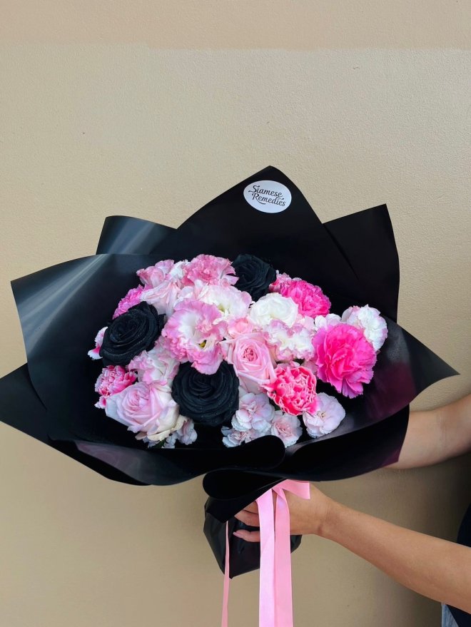 A dramatic bouquet of black, pink, and white roses with carnations and lisianthuses in black wrapping.