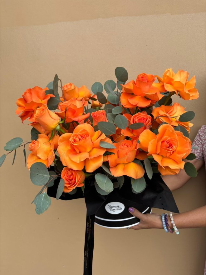 A vivid black hatbox bouquet featuring bright orange roses and eucalyptus leaves.