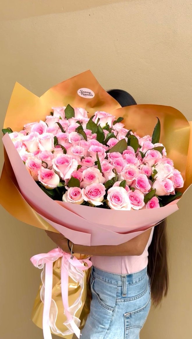 A large bouquet of pink roses wrapped in blush pink and gold paper.