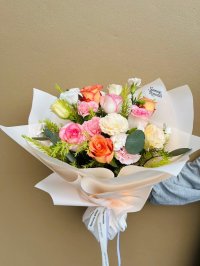 A cream-wrapped bouquet featuring coral, pink, and cream roses with carnations and lisianthuses.