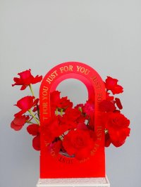A dramatic red floral box with red roses and carnations arranged inside a “Just for You” red arch box.
