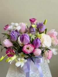 Arrangement of purple tulips, blush peonies, white orchids, pink lisianthus, and white carnations in a hatbox with lilac ribbon