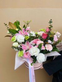 A vivid hatbox arrangement with pink lilies, roses, lisianthuses, and carnations with fresh greenery.
