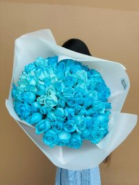 A large bouquet of vibrant blue roses wrapped in white paper.