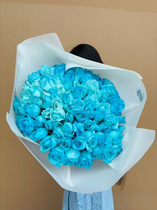 A large bouquet of vibrant blue roses wrapped in white paper.