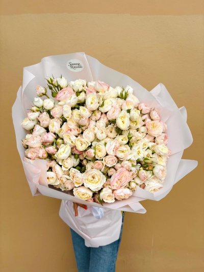 A pastel bouquet of blush pink and cream roses wrapped in soft white paper.