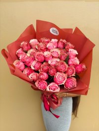A bouquet of vibrant pink roses wrapped in deep crimson red paper.