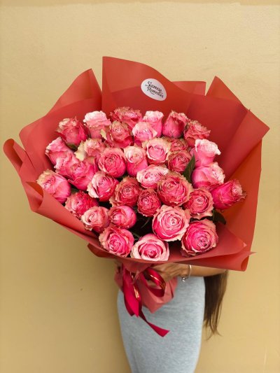 A bouquet of vibrant pink roses wrapped in deep crimson red paper.