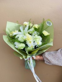A green-themed bouquet with white lilies, cream carnations, and chrysanthemums wrapped in green paper.