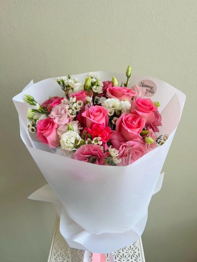 Bouquet of pink roses, white wax flowers, pink lisianthus, and carnations wrapped in white paper with a pink ribbon
