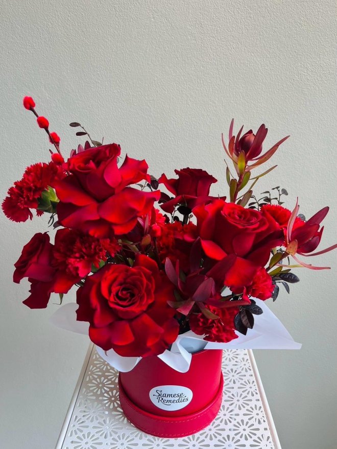 Bouquet of red roses, maroon chrysanthemums, red carnations, waxflowers, and dark foliage wrapped in red and burgundy paper with satin ribbons