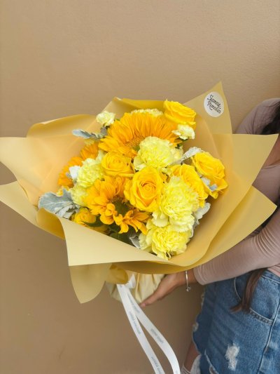 A cheerful bouquet of yellow sunflowers, roses, and carnations wrapped in golden paper.