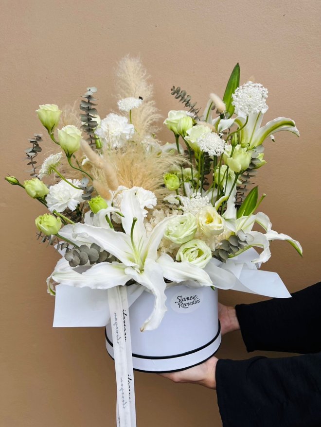 Pure white lilies, lisianthus, carnations, queen anne’s lace, eucalyptus, and soft pampas grass in a white hat box.