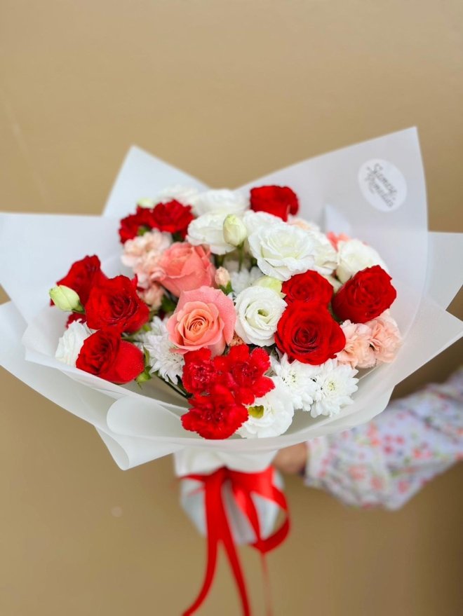 A bouquet with red and pink roses, white lisianthus, carnations, and chrysanthemums tied with red ribbon.