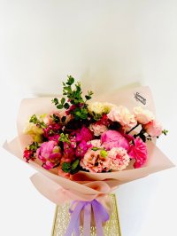 A vivid pink bouquet with peonies, carnations, lisianthuses, and roses wrapped in soft blush paper with a lavender ribbon.