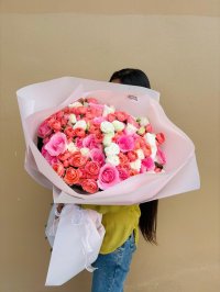 A large blush-wrapped bouquet of pink, coral, and white roses.