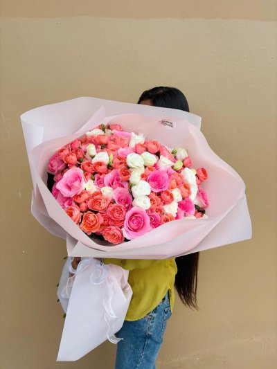 A large blush-wrapped bouquet of pink, coral, and white roses.