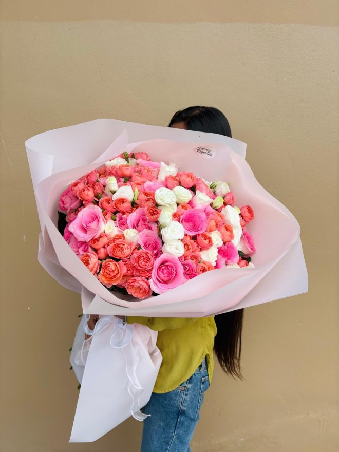 A large blush-wrapped bouquet of pink, coral, and white roses.