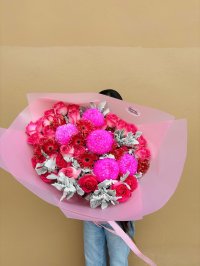 A bold bouquet of pink pompom chrysanthemums, red gerberas, and roses with silver foliage, wrapped in pink paper.