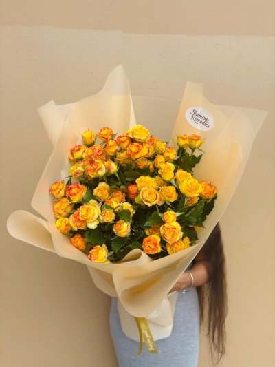 A bouquet of vibrant yellow and orange spray roses wrapped in soft cream paper.
