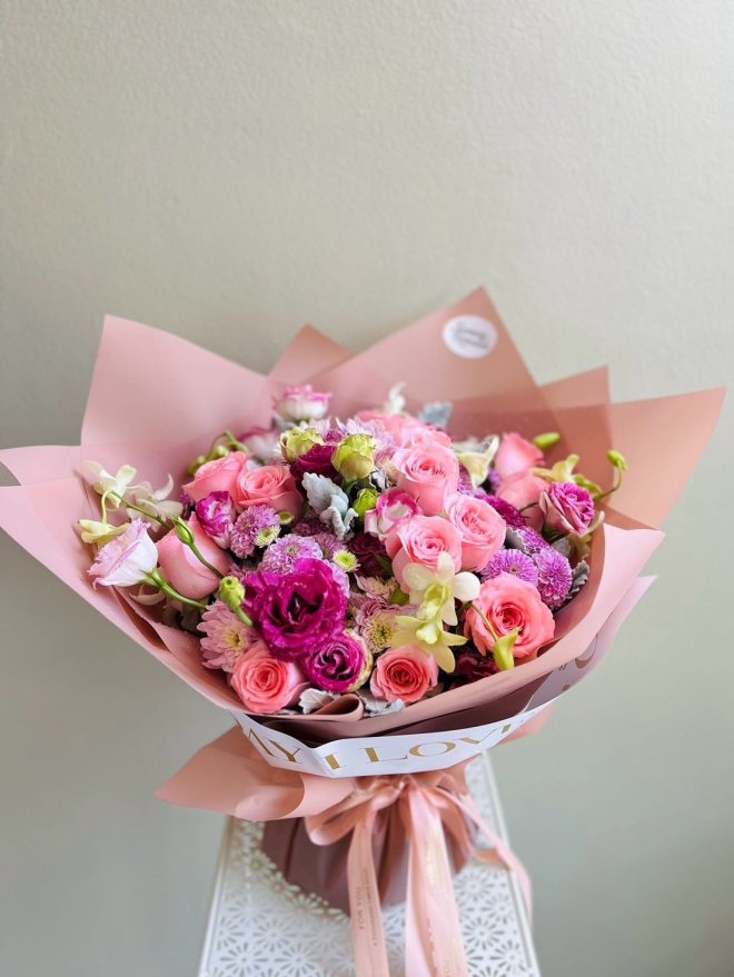 Bouquet of pink roses, purple lisianthus, chrysanthemums, and orchids wrapped in pink paper with satin ribbon