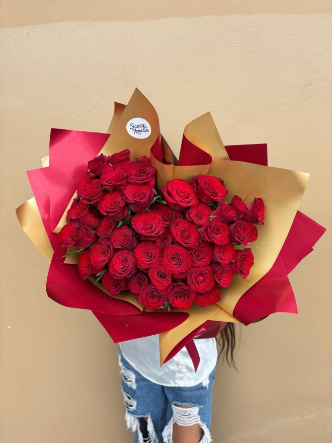 A grand bouquet of vibrant red roses wrapped in gold and red paper.