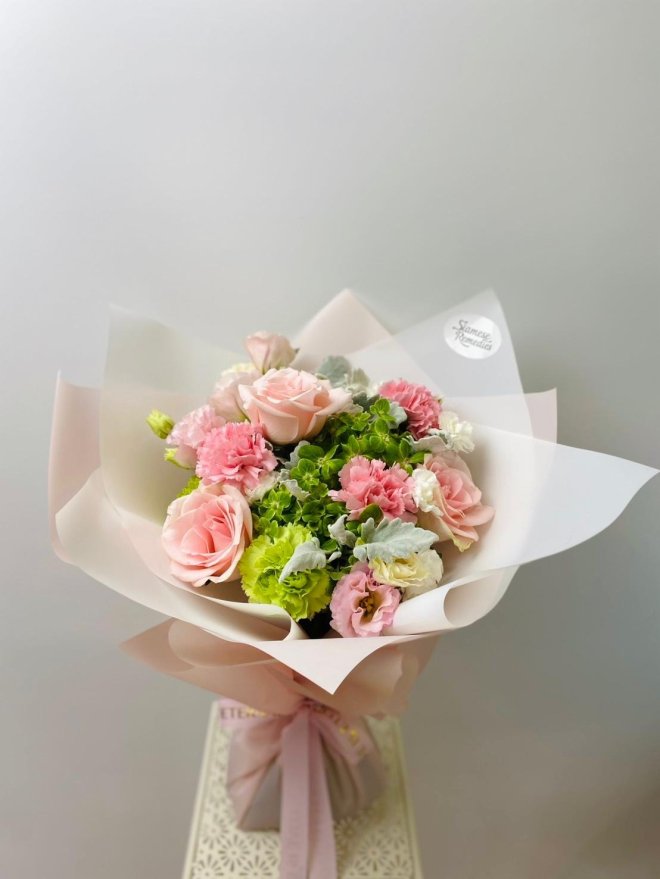 A pastel bouquet featuring pink roses, green hydrangeas, lisianthuses, and carnations wrapped in soft blush paper.