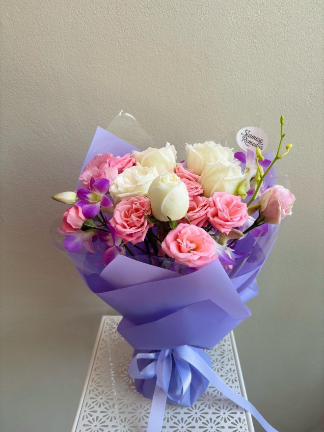Pastel bouquet with white roses, pink spray roses, lisianthus, and purple orchids wrapped in lavender paper