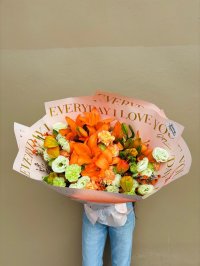 A bouquet of orange lilies, carnations, and green lisianthus wrapped in decorative “Everyday I Love You” paper.