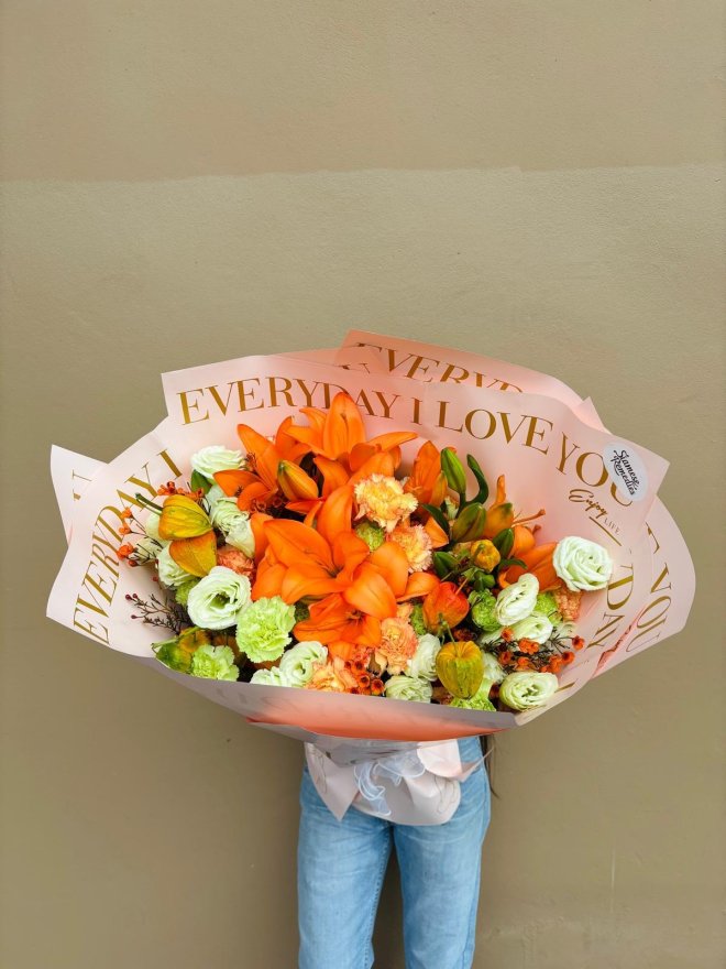A bouquet of orange lilies, carnations, and green lisianthus wrapped in decorative “Everyday I Love You” paper.