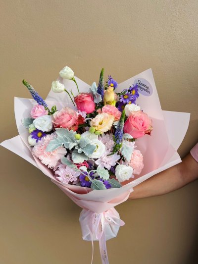 A pastel-hued bouquet blooming with soft pink roses, lavender asters, creamy lisianthus, and lilac chrysanthemums. 