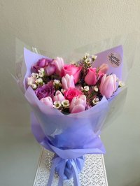 Bouquet of pink tulips, blush and lilac roses, and white wax flowers wrapped in lavender paper with matching ribbon